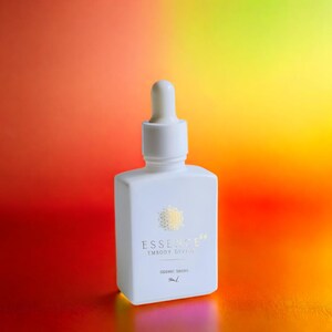 May include: A white square bottle with a dropper top, featuring gold text that reads "ESSENCE 64 EMBODY DIVINE" and "SIDERIC DROPS". The bottle is set against a gradient background of red, orange, and yellow.