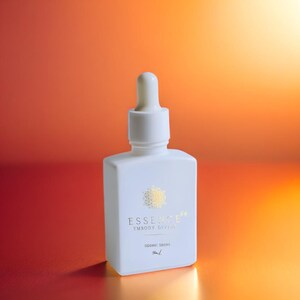 May include: A white, square-shaped bottle with a dropper top. The bottle has gold text that reads "ESSENCE" and "EMBODY DIVINE". The bottom of the bottle reads "SIDERIC DROPS" and "5ml". The background is a gradient of orange and red.