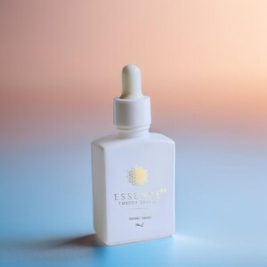 May include: A white square bottle with a dropper top. The bottle has gold text that reads "ESSENCE EMBODY DIVINE" and "SIDDIC DROPS". The background is a gradient of blue, peach, and orange.