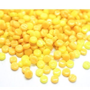 May include: A pile of small, round, yellow and orange glass beads. The beads are scattered on a white surface.