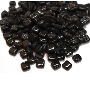 May include: A pile of black square glass tiles. The tiles are shiny and have a smooth surface.