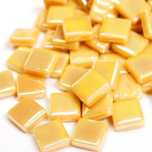 May include: A pile of small, square, iridescent gold glass tiles. The tiles are smooth and have a slight sheen.