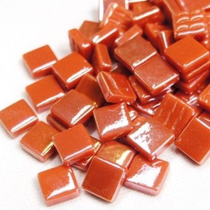 Pu&ograve; includere: Un mucchio di piccole piastrelle di vetro quadrate di colore arancione con una finitura lucida.