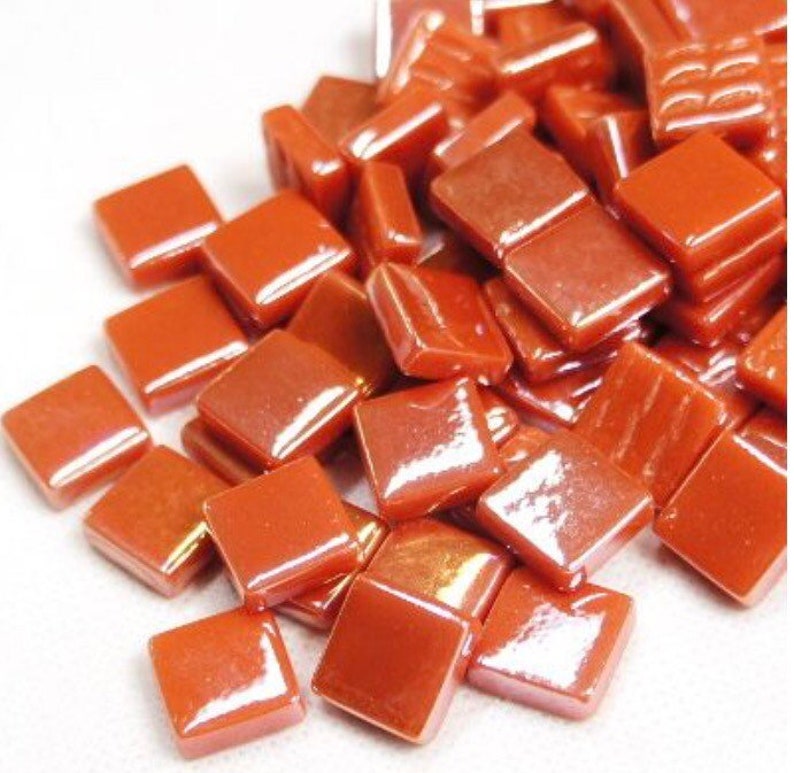 Pu&ograve; includere: Un mucchio di piccole piastrelle di vetro quadrate di colore arancione con una finitura lucida.