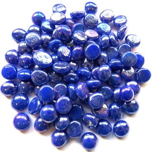 May include: A large pile of iridescent blue glass pebbles. The pebbles are smooth and round, and they have a slight shimmer to them.