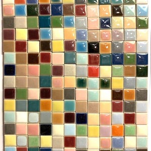 May include: A grid of small, square ceramic tiles featuring a diverse array of glossy, solid colors including shades of blue, green, red, yellow, pink, brown, black, white, and gray, arranged in a uniform rectangular pattern.
