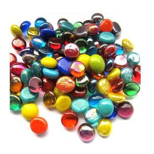 May include: A collection of colorful, smooth glass pebbles in various sizes and shades. The assortment includes red, orange, yellow, green, blue, and purple hues. These decorative stones have a glossy finish and are arranged against a white background.