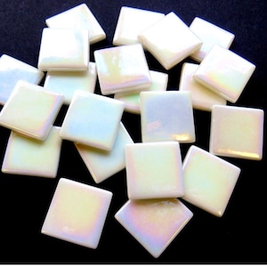 May include: A collection of iridescent, square-shaped mosaic tiles. The tiles have a pearlescent finish that reflects a spectrum of colors. The tiles are scattered, showcasing their glossy surface and potential for craft projects.