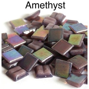 May include: A pile of iridescent square tiles in shades of purple, brown, and green. The tiles have a glossy finish and are scattered on a white surface. The word "Amethyst" is written in black letters at the top.