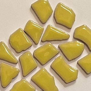 May include: A collection of yellow ceramic mosaic tiles in various irregular shapes. The tiles are glossy and have a smooth surface.