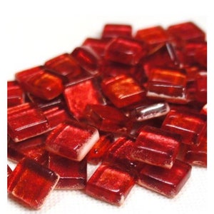 May include: A pile of small, square, red glass tiles with a slight shimmer. The tiles are about 1 inch by 1 inch.