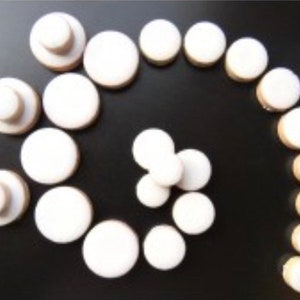 May include: A collection of white round buttons arranged in a spiral pattern on a black surface. The buttons are various sizes and are made of a smooth, white material.