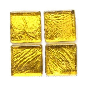 May include: Four square gold glass tiles with a textured surface. The tiles are approximately 1 inch by 1 inch.