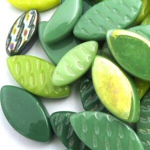May include: A collection of green leaf-shaped glass beads in various shades, including light and dark greens, and a few with textured surfaces. Some beads have a yellow hue.