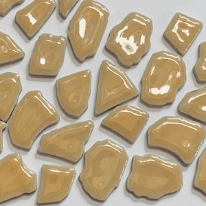 May include: A collection of irregular shaped ceramic tiles in a light beige color. The tiles are glossy and have a slightly translucent appearance.