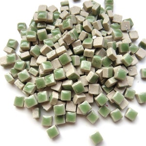May include: A pile of small, square ceramic tiles in shades of green and beige. The tiles are glossy and have a slightly uneven surface.