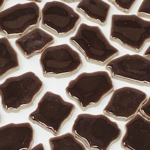 May include: A collection of brown ceramic mosaic tiles in various irregular shapes. The tiles have a glossy finish and are arranged on a white background.