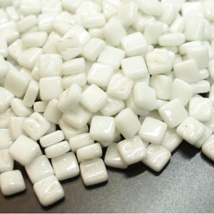 May include: A pile of small, white, square glass tiles. The tiles are smooth and glossy.