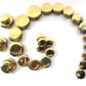 May include: A collection of small, shiny, golden-colored metal buttons arranged in a spiral and scattered on a white surface. The buttons have a slightly domed shape and reflect light, creating highlights and shadows.