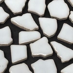 May include: White ceramic mosaic tiles with irregular shapes and edges. The tiles are arranged in a random pattern on a black background.