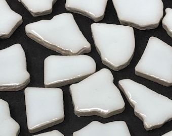 May include: White ceramic mosaic tiles with irregular shapes and edges. The tiles are arranged in a random pattern on a black background.