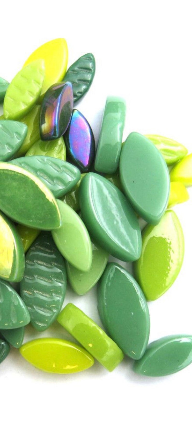 May include: A collection of green glass beads in various shades, including lime, olive, and emerald. Some beads have a leaf shape, while others are rectangular or oval. A few beads have an iridescent sheen.