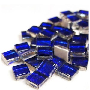 May include: A pile of small, square, iridescent blue glass tiles with silver backing. The tiles are perfect for crafting and mosaic projects.