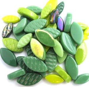 May include: A collection of green glass beads in various shades, including light and dark greens, and a few with iridescent finishes. The beads are leaf-shaped and rectangular, suitable for jewelry making or craft projects.