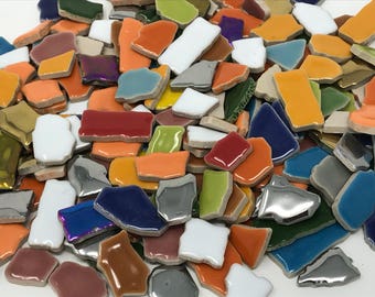 May include: A collection of colorful ceramic tile pieces in various shapes and sizes. The tiles are in shades of blue, green, red, orange, yellow, white, and silver.