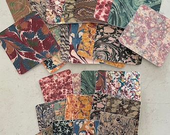 May include: A collection of square tags with marbled paper designs in various colors. The tags feature a hole at the top for hanging. Colors include burgundy, teal, brown, and cream, with swirling patterns.
