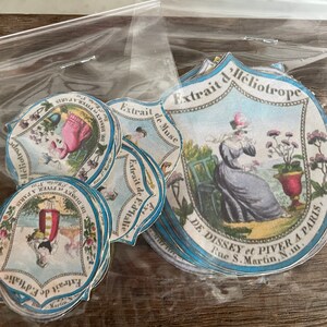 May include: A stack of vintage paper labels with blue and white borders. The labels feature illustrations of women in dresses and the text "Extrait de Heliotrope" and "DE DISSEY et PIVER A PARIS, Rue S. Martin, N.11."