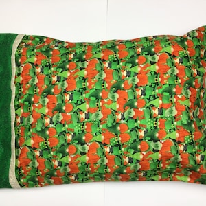 May include: Rectangular pillowcase featuring a repeating pattern of orange-haired gnomes wearing green hats and outfits. The pillowcase has a green border on one side with a light beige stripe separating the two fabrics. The pillow is a festive item.