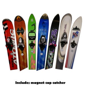 May include: A collection of repurposed vintage skis transformed into bottle openers. Each ski features a unique design, including graphics and branding. The openers are mounted with a bottle opener mechanism and a magnet cap catcher.