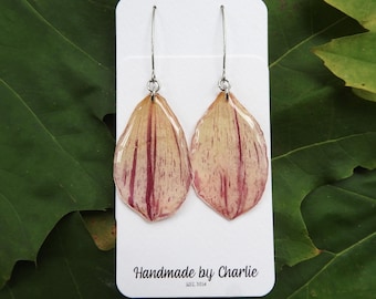 May include: A pair of handmade earrings with a petal design in cream and burgundy hues. The earrings hang from silver-coloured hooks and are presented on a white card. The card has the text "Handmade by Charlie EST. 2014".