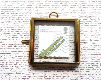 May include: A square brass frame containing a postage stamp featuring a green crocodile illustration. The stamp includes the text The Enormous Crocodile by Roald Dahl, illustrated by Quentin Blake, and a silhouette of Queen Elizabeth II with 1st class.