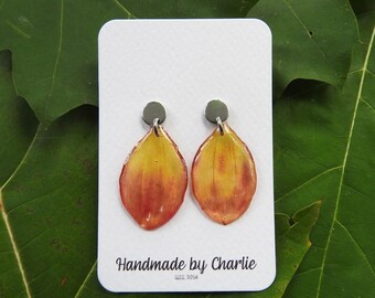 May include: Handmade teardrop earrings with a yellow to red gradient. The earrings are attached to small, round silver studs. The card reads "Handmade by Charlie EST. 2014." The earrings are displayed on a white card.