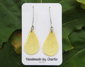 May include: A pair of handmade yellow teardrop earrings with silver hooks. The earrings are presented on a white card with the text "Handmade by Charlie" and the year "est. 2014". The background features green leaves.