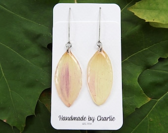 May include: A pair of handmade earrings with pale yellow and pink petal-shaped pendants hanging from silver-coloured hooks. The earrings are displayed on a white card with the text "Handmade by Charlie EST. 2014".