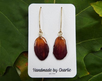 May include: Handmade earrings with brown and orange petal-shaped pendants hanging from gold-tone hooks. The earrings are presented on a white card with the text "Handmade by Charlie EST. 2014".