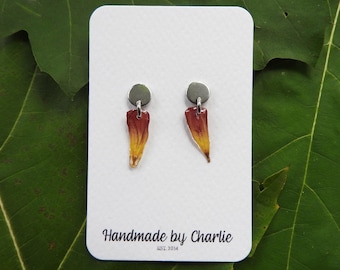 May include: Handmade earrings with silver studs and teardrop pendants in red and yellow. The earrings are presented on a white card with the text "Handmade by Charlie EST. 2014".