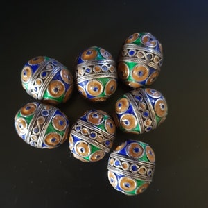May include: Eight decorative beads with intricate patterns in shades of blue, green, and gold. The beads are oval-shaped and have a metallic finish.