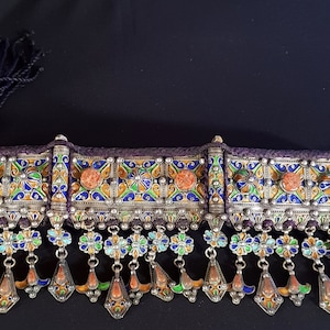 Op de afbeelding: Een zilveren en geëmailleerde ketting met een geometrisch ontwerp en koraalaccenten. De ketting heeft een centrale band met daaruit hangende kwastjes.