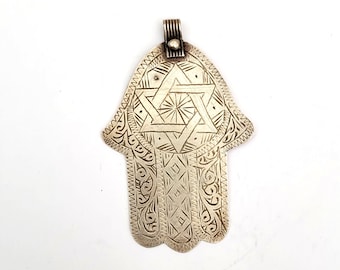 Pode incluir: Um pingente de prata em forma de mão de hamsa com um design detalhado da estrela de David.