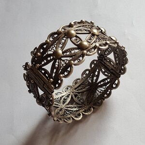May include: A silver filigree bracelet with a hinged clasp. The bracelet is made of delicate, intricate metalwork and features a floral design.