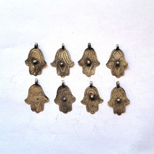 Könnte beinhalten: Acht silberne Hamsa-Hand-Anhänger mit filigranen Designs. Jeder Anhänger hat eine kleine Perle in der Mitte der Handfläche.