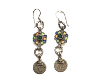 Pode incluir: Um par de brincos de prata com flores de esmalte verde, azul e amarelo e um pendente de moeda. A moeda tem escrita árabe.