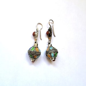May include: A pair of silver dangle earrings with colourful enamel detailing. The earrings feature a round, multi-coloured enamel bead with a silver wire design. The beads are a mix of blue, green, yellow, and orange.