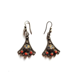 May include: A pair of silver earrings with a teardrop shape and a colourful enamel design. The earrings have a small red coral bead at the bottom.