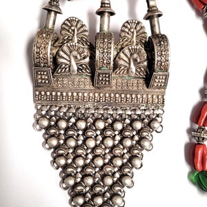May include: A silver pendant necklace with a detailed design of peacocks and a chain fringe. The necklace is made of silver and has a traditional Indian design.