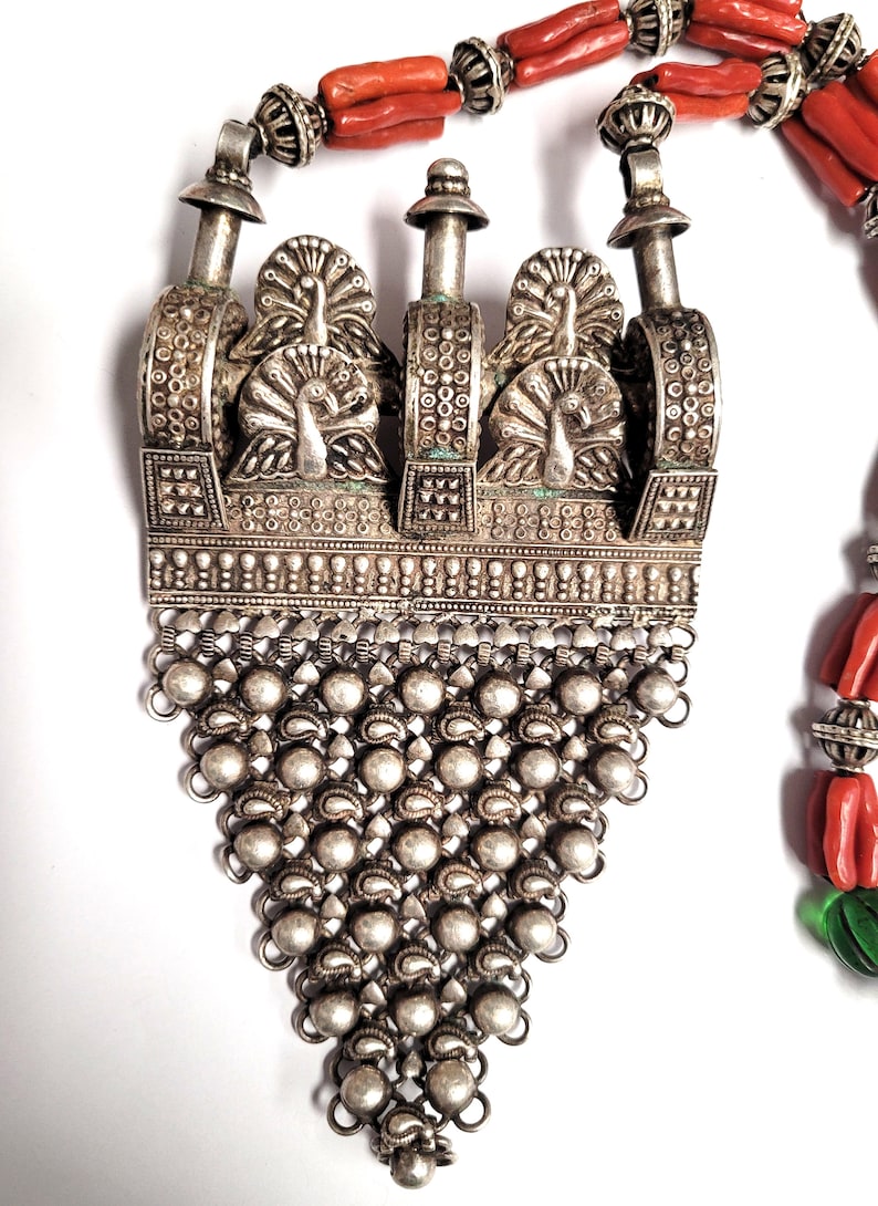 May include: A silver pendant necklace with a detailed design of peacocks and a chain fringe. The necklace is made of silver and has a traditional Indian design.